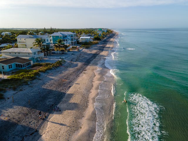 aerial view of waves washing up the beach near houses and palm trees 